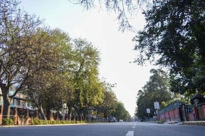 Empty road amidst trees against sky in city