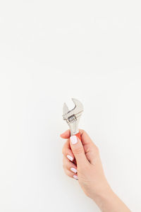 Cropped hand of woman holding wrench against white background