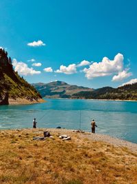 Men fishing in lake against mountains and sky