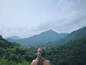 Rear view of woman looking at mountains while standing against cloudy sky