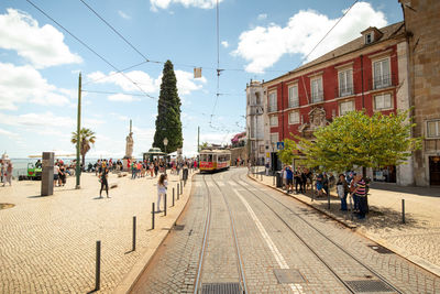 People on railroad tracks in city against sky