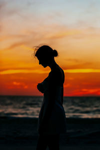 Silhouette woman standing at beach during sunset