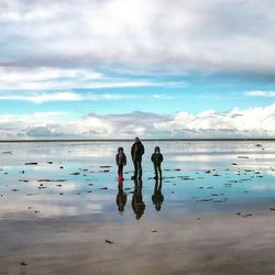 Family standing on wet shore at beach against sky