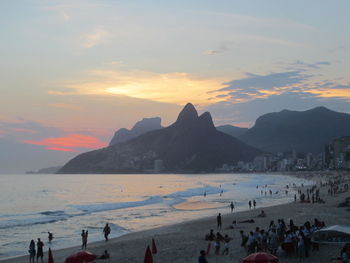 People enjoying vacation at beach with mountain in background during sunset