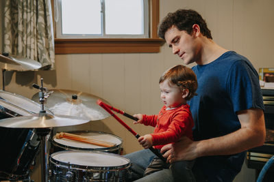 Father holding baby son playing drum at home