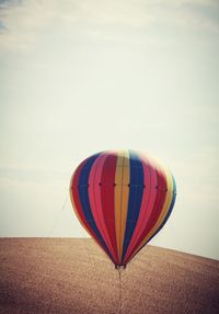 Hot air balloon flying over field against sky