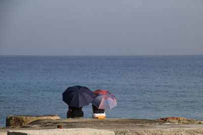 Rear view of couple with umbrellas sitting against sea