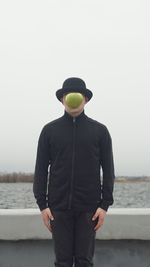 Man by water with apple in front of face