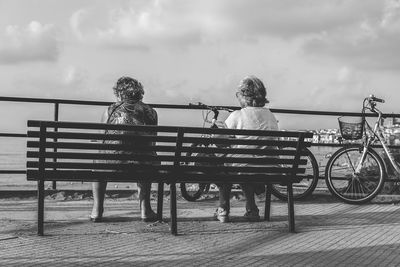 Rear view of people sitting on bench against sky