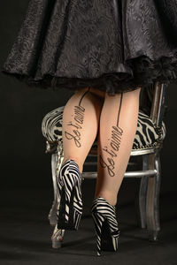 Low section of woman with tattoos wearing high heels against black background