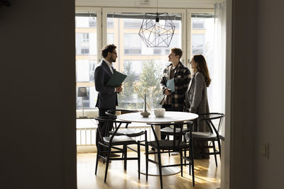 Multiracial couple discussing with salesman while standing at home