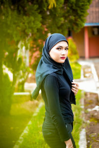 Side view of young woman standing against plants