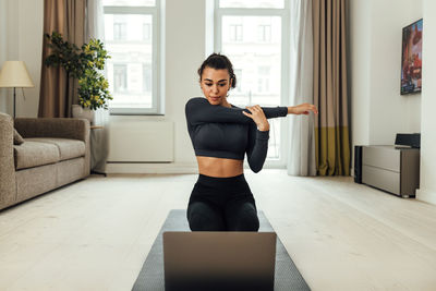 Beautiful woman stretching at home while looking at laptop