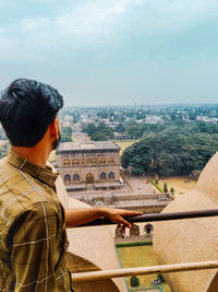 Rear view of man looking at cityscape against sky