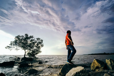 Man standing on rock by sea against sky