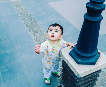 High angle view of cute boy looking up while standing by pole on footpath