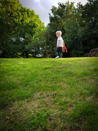 Portrait of boy holding toys while walking on grassy field at park