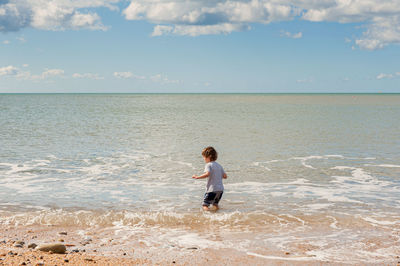 Cute boy standing on shore against sky