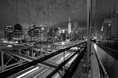 Brooklyn bridge by illuminated city skyline against sky at night