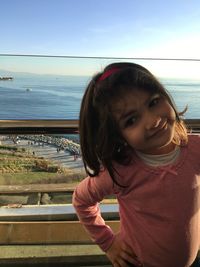 Cute girl standing by railing against sky