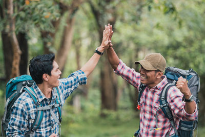 Young man with arms raised standing against trees