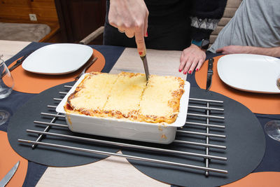 Woman cut with knife hot tasty home baking lasagna in ceramic casserole dish