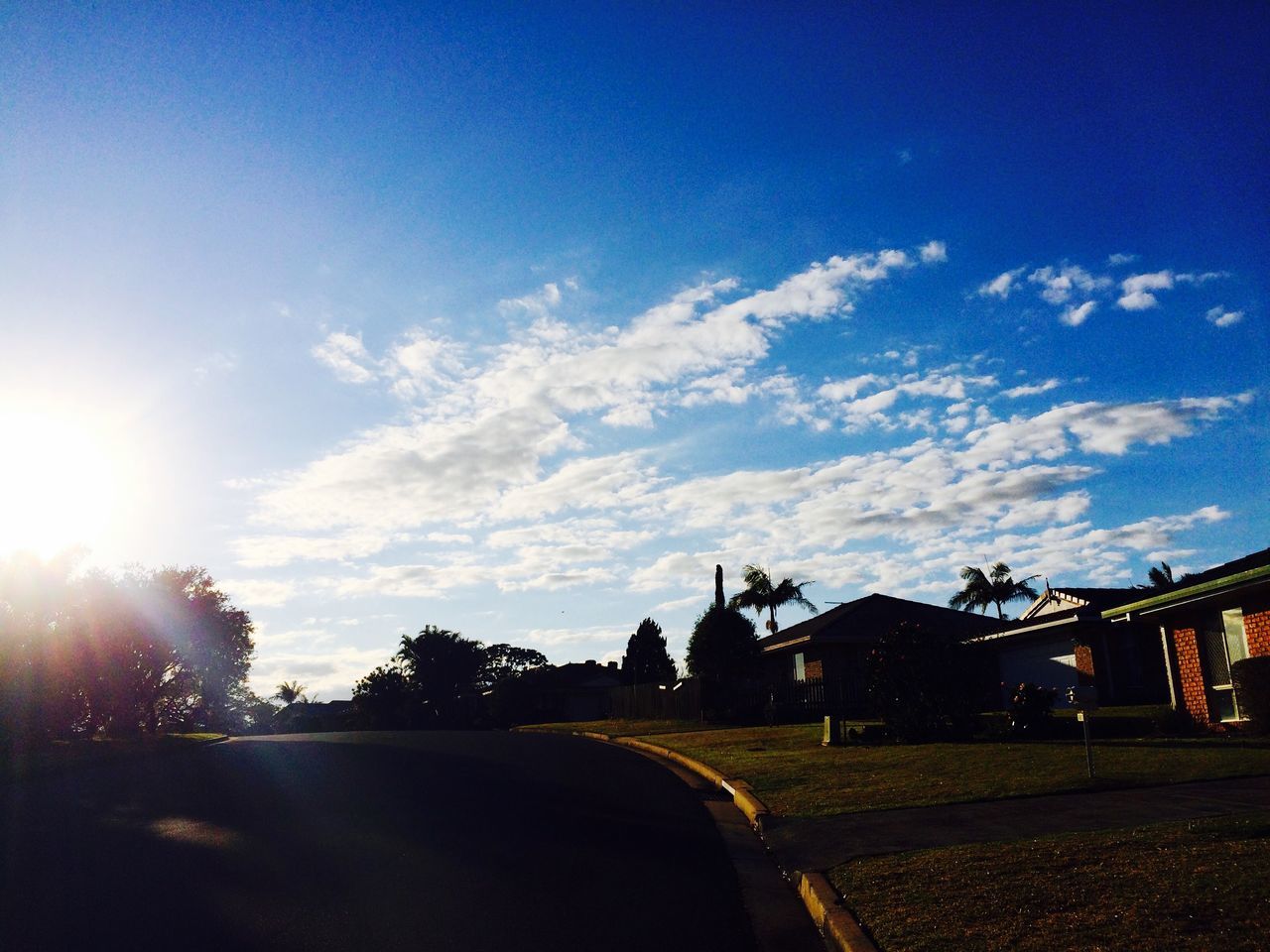 sky, road, transportation, tree, sunlight, sun, sunbeam, cloud - sky, blue, street, car, landscape, building exterior, lens flare, cloud, the way forward, built structure, nature, silhouette, outdoors