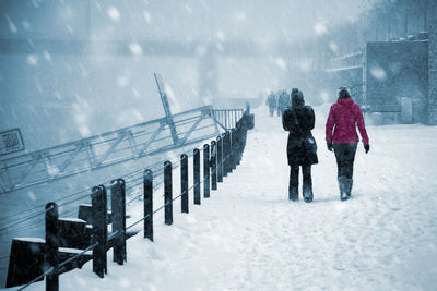 Rear view of people walking on snow covered bridge during winter