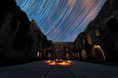 Low angle view of star trails over old ruins at night