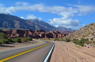 Empty road leading towards mountains against sky