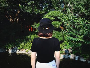 Rear view of woman standing by lake in forest