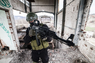 Army soldier aiming rifle while standing in building