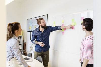 Businessman explaining adhesive note to colleagues in creative office