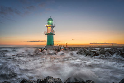 Lighthouse by sea against sky during sunset