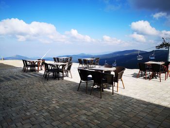 Empty chairs and tables at beach against sky