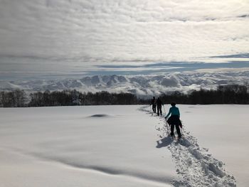 People skiing on snowy field against cloudy sky