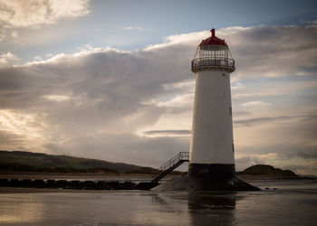 Lighthouse by sea against sky during sunset