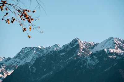 Low angle view of snowcapped mountains against clear blue sky