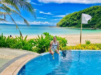 Man siting on infinity pool at beach against sky