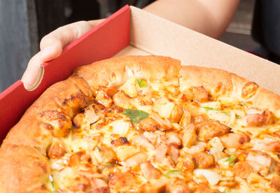 Close-up of hand holding pizza in box 