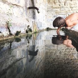 Side view of shirtless boy putting hand in trough