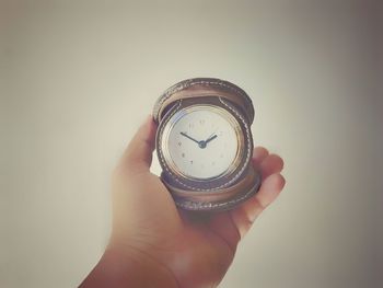 Close-up of hand holding clock against white background