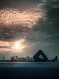 Woman lying down on snow against sky during sunset