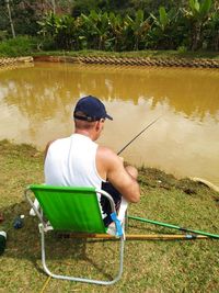 Rear view of man sitting on chair by lake