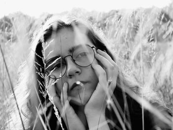 Close-up portrait of young woman with hands on chin amidst plants