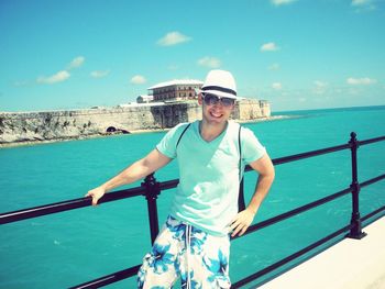 Portrait of young man standing on railing against sea