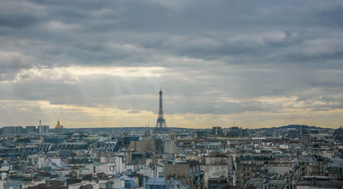 Distant view of eiffel tower amidst cityscape against cloudy sky