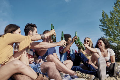 Happy friends toasting beer while sitting at beach