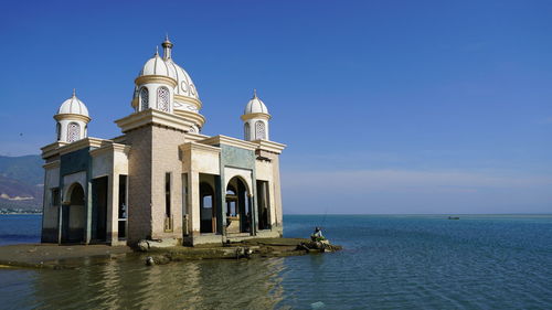 Building by sea against clear blue sky