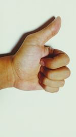 Cropped hand gesturing thumbs up sign over white background